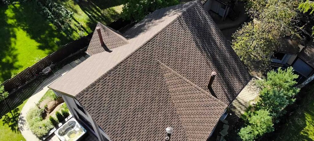 A close-up view of a partially shingled roof showing black underlayment being installed by gloved hands.